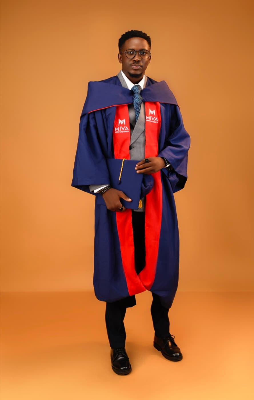 Blessing Ajala in navy and red Miva Open University robes, holding his mortarboard in both hands